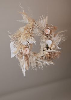 a dried wreath hanging from the ceiling with flowers and feathers attached to it's sides