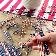 someone is holding some patriotic paper straws on a table with an american flag in the background