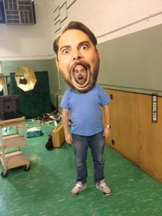 a man standing in front of a large cardboard cut out of him's face