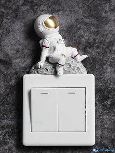 an astronaut doll is sitting on top of a light switch cover in the shape of a spaceman