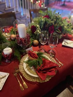 the table is set for christmas dinner with red cloths and greenery on it