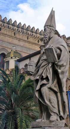 a statue of a man with a book in front of a building and palm tree