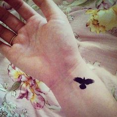 a woman's hand with a small black bird tattoo on her left wrist,