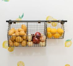 two metal baskets filled with fruit sitting on top of a white wall next to lemons