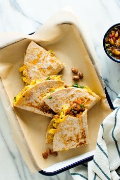 three quesadillas on a plate next to a bowl of beans and a napkin