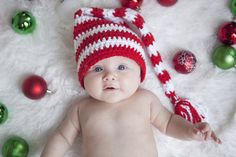 a baby wearing a red and white crocheted hat laying next to christmas ornaments