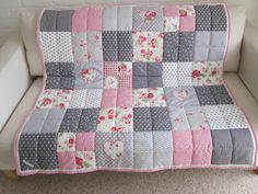 a white couch with a pink and gray patchwork quilt on it's back