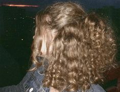 the back of a woman's head with long curly hair and blue denim jacket