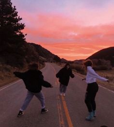 three people skateboarding down an empty road at sunset