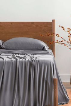 there is a bed with gray sheets and pillows on the headboard, next to a vase with red flowers