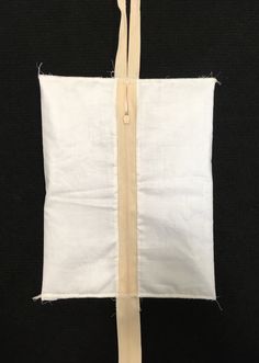 a piece of white fabric with a zipper on the front and back of it, hanging from a black background