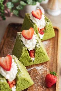 three pieces of green cake with strawberries and whipped cream on top sitting on a cutting board