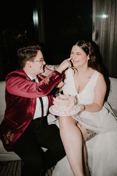 a man feeding a woman a piece of cake on top of her lap while sitting next to him