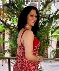 a woman in a red dress standing next to a palm tree