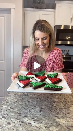 a woman holding a plate with decorated cookies on it in the shape of christmas trees