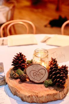 a wooden slice with pine cones and a mason jar on it sitting on a table