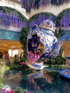 an elaborately decorated teapot is in the middle of a garden filled with purple flowers