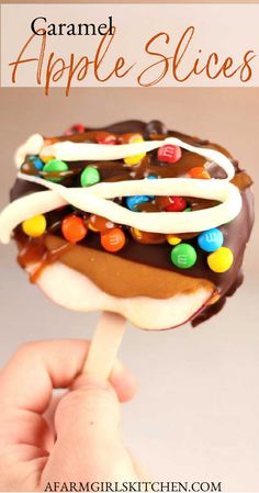 a hand holding an ice cream covered caramel apple slice with chocolate and candy on top