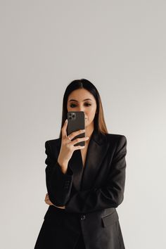 a woman in a suit taking a selfie with her cell phone while standing against a white background