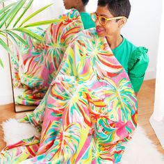 two people sitting on the floor wrapped in colorful blankets and smiling at each other with palm tree behind them