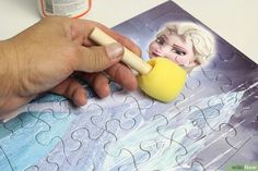 a person holding a sponge next to a piece of jigsaw puzzle with an image of frozen queen on it