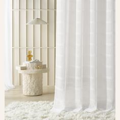 a white shower curtain in a bathroom next to a table with a lamp on it