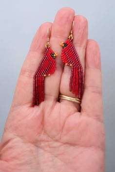 a pair of red beaded bird earrings on a person's hand