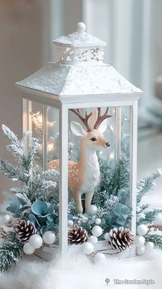 a white lantern with a deer figurine in it and pine cones on the side