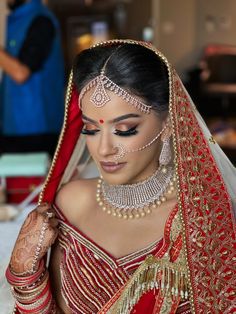 a woman in a red and gold bridal outfit is looking down at her hands