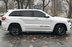 a white jeep is parked in a parking lot with trees and leaves on the ground