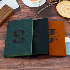 three notebooks sitting on top of a wooden table next to a cup of coffee