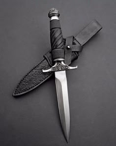 a large knife with a black handle on a gray surface, next to a leather sheath