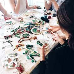 a group of people sitting around a table covered in crafting supplies and beading