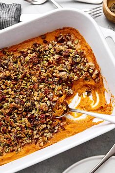 a white casserole dish filled with sweet potato casserole topped with nuts