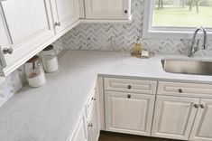 a kitchen with white cabinets and marble counter tops