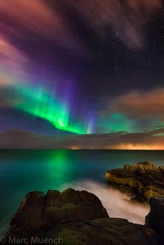 an aurora bore over the ocean with rocks and stars in the night sky above it