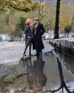 two figurines are standing in the middle of a puddle, one is wearing a suit and tie