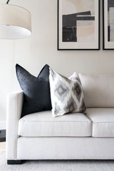 a white couch with two black and gray pillows on it's back, in front of three framed pictures