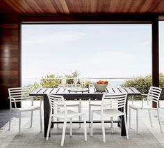 an outdoor table with chairs and a bowl of fruit on it in front of a large window