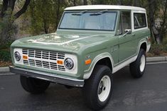 an old green and white truck parked on the side of the road in front of some trees