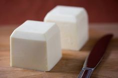 two cubes of cheese sitting on top of a wooden cutting board next to a knife