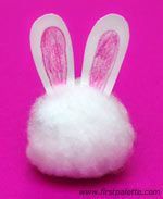 a white fluffy ball with bunny ears on it's side, sitting in front of a pink background