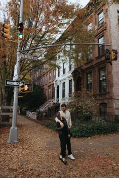 a man and woman standing in the middle of a leaf covered street next to a traffic light