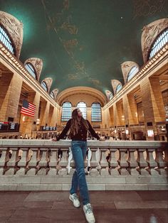 a woman is standing in the middle of a train station looking up at the ceiling