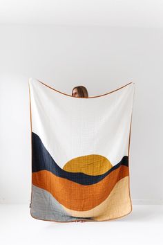 a woman is holding up a quilt with an orange, blue and yellow design on it