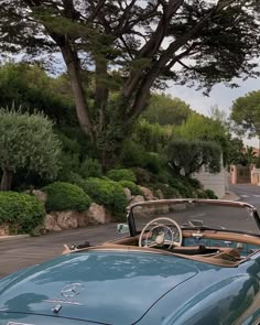 an old blue convertible car parked on the side of the road next to a tree