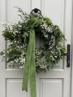 a wreath with white flowers and greenery hangs on a door