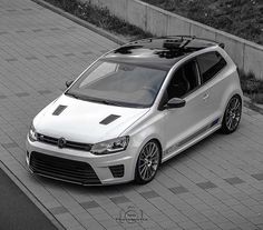 a white car parked on top of a brick road next to a wall and grass