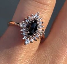 a woman's engagement ring with an oval black diamond surrounded by small white diamonds