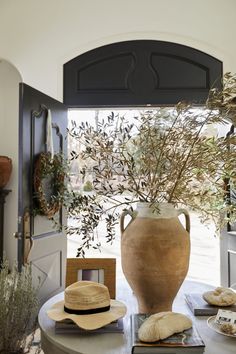 a vase and hat on a table in front of an open door with a tree